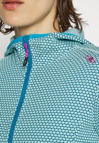 Giacca con cappuccio azzurra chiara con un motivo a rete. Presenta una zip frontale con un tirante rosa e un piccolo logo ricamato in rosa.