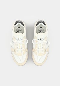 Sneakers albe și bej, cu un amestec de materiale netede și texturate, vârful rotund, accente negre contrastante și șireturi plate albe.