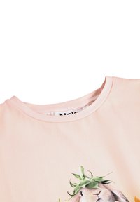 Svetlo roza majica s okroglim izrezom, ki ima natisnjen vzorec zajca, ki nosi zelene liste kot klobuk.