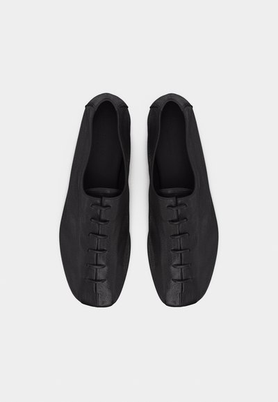 Ζευγάρι μαύρα δερμάτινα παπούτσια με φλατ σόλα, τετράγωνες μύτες και ελάχιστες ραφές, από ψηλά σε λευκό φόντο.