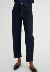 Donkerblauwe hoge taille denim jeans met een recht gesneden ontwerp, contrasterende oranje stiksels en vijf zakken.