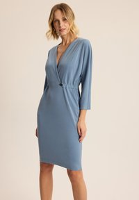 Niebieska, dopasowana sukienka z gładkiego materiału, z dekoltem w serek, rękawami o długości trzech czwartej i guzikiem w talii.
