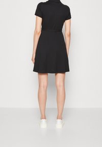 Czarna sukienka z krótkim rękawem, z kołnierzykiem, dopasowaną talią i rozkloszowanym dołem. Połączona z białymi trampkami. Gładki bawełniany materiał, minimalistyczny design.