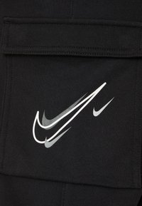Černá látka se výrazným bílým logem Swoosh Nike a dalšími menšími designy Swoosh, texturovaná švy.