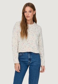 Crochet-style, cream sweater with colorful speckles, round neckline, and ribbed hem. Paired with high-waisted blue jeans.