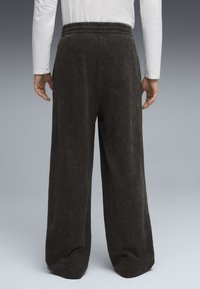 Mørkegrå, brede sweatpants med elastisk talje. Teksturen ser blød ud med en subtil glans. Ingen lommer synlige. Casual design.