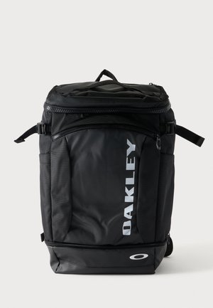 Sac à dos Oakley rectangulaire noir avec poignée supérieure, sangles latérales réglables, poche avant zippée et logo blanc sur le panneau avant.