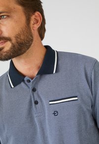 Marineblauwe polo met een gestructureerde stof, een drieknopenlijn, witte kraagstrepen en een smalle zak met een gestreepte accentuering.