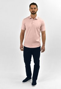 Lichtroze polo met korte mouwen, voorzien van een drieknoopsluiting. Gekleed met marineblauwe broek en casual instapschoenen.