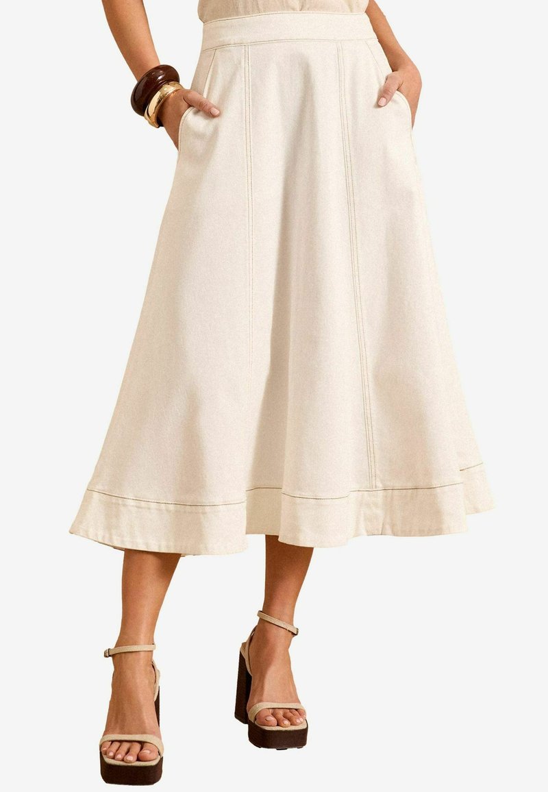 Beige midi rok met uitlopende vorm en zakken, met zichtbare naden en een geaccentueerde zoomlijn. Gepaard met lichtbeige plateauhakken.