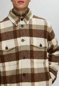 Uld flannel skjortejakke i brun, creme og grå ternet med knaplukning, to brystlommer og høj krave.