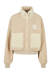 Giacca in fleece beige con colletto alto, chiusura con zip, due tasche frontali e polsini a costine. Presenta un logo sul lato sinistro del petto.