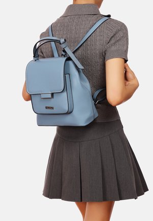 Zaino in pelle azzurro chiaro con chiusura a patta, forma strutturata, spallacci regolabili e cuciture a contrasto. I dettagli includono un piccolo logo in metallo.