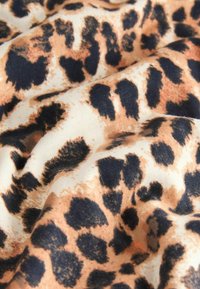 Leopardenmusterstoff mit einer sanften Textur, einem beigen Grund, dunklen braunen Flecken und hellbraunen Akzenten in einem gekrümmten Muster.