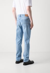 Lyseblå jeans med rett passform, preget av en lærlapp i livet og to baklommer, kombinert med svarte fottøy.