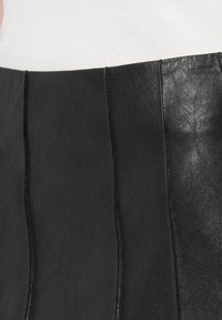 Black leather skirt featuring horizontal paneling with visible stitching. Smooth texture with a slight sheen. Tailored design and fitted shape.