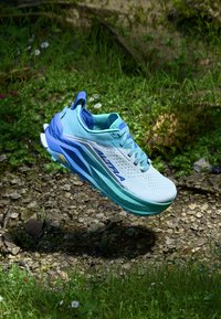 Šviesiai mėlynas sportinis batelis su tinklelio viršumi, gradientine žalsvai mėlyna padu ir baltais akcentais. Yra raišteliai, skylutės ir prekės ženklas šone.