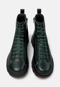 Botas de tobillo de cuero verde con un acabado suave, puntera redonda, cordones delanteros y cierre de cremallera. Suela de goma con un agarre texturizado.
