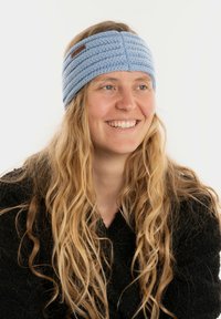 Fascia per la testa di colore azzurro chiaro, lavorata a maglia, con un motivo intrecciato e una piccola etichetta in pelle marrone del marchio. Morbida ed elastica per garantire comfort.