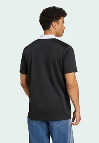 Sort polo t-shirt med hvid krave. Korte ærmer, glat tekstur. Båret med blå denim jeans med sidelange striber. Bagview.