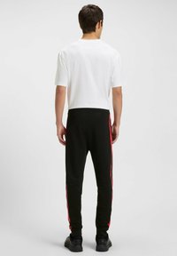Sorte joggers med røde sidestriber, parret med en ensfarvet hvid t-shirt med korte ærmer. Designet er afslappet med en løs pasform og elastisk talje.