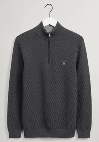 Pull en tricot gris avec col montant, demi-zip et motif texturé. Présente un petit logo sur la poitrine et des poignets côtelés.