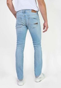 Jeans de mezclilla de color azul claro con un ajuste slim, que cuentan con bolsillos traseros y un acento de cuero marrón cerca de la cinturilla. Textura suave y piernas rectas.
