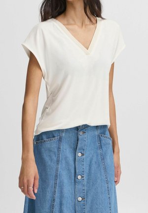 Světle béžový top s krátkými rukávy a výstřihem do V s žebrovaným lemováním, doplněný modrou džínovou sukní se zapínáním na knoflíky a bočními kapsami.