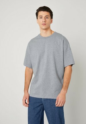 T-shirt gris à manches courtes avec un col rond, coupe décontractée, en coton doux et texture lisse, associé à un pantalon en denim bleu.