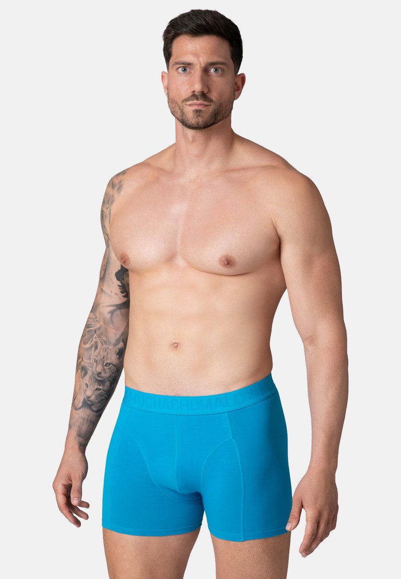 Niebieskie bokserki z markową elastyczną taśmą, o gładkiej fakturze i dopasowanym kroju, prezentowane na mężczyźnie bez koszuli.