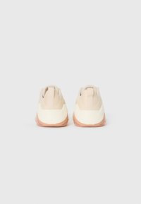 Lichtbeige sport schoenen met een gladde stoffen bovenkant, een gestructureerde hak en een witte tussenzool. Roze rubberen buitenzool. Minimalistisch ontwerp, geen merknaam.