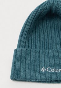 Berretto lavorato a maglia color teal con texture a coste. Presenta un risvolto e il logo "Columbia" ricamato in bianco sulla parte frontale.