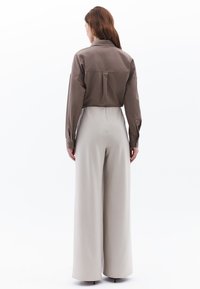 Camicia corta marrone con colletto e polsini a bottone, abbinata a pantaloni beigi larghi a vita alta. Tessuto liscio e vestibilità su misura.