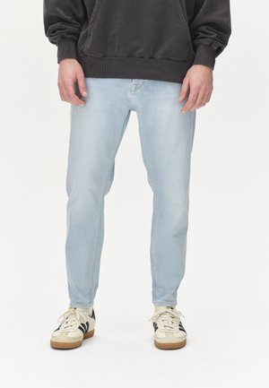 Lichtblauwe denim jeans met een slim fit, met een vijf-pocket ontwerp en een subtiele vervaging, gecombineerd met crèmewitte en zwarte sneakers.