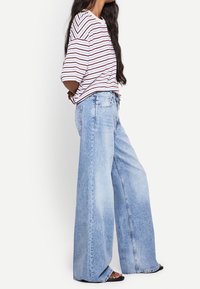 Randig kortärmad skjorta i vitt, rött och marinblått; tillsammans med vida ljusblå denimjeans med en blekt tvätt och avslappnad passform.