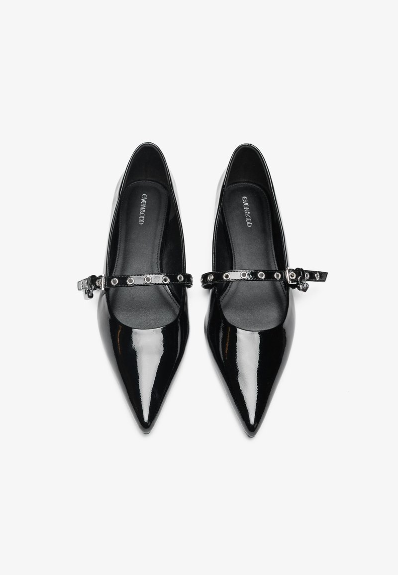 Escarpins en cuir verni noir avec un bout pointu et une fine sangle réglable avec des accents en métal circulaire. Fini lisse et brillant.