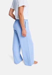 Pantalones de pierna ancha de color azul claro, fabricados en un tejido suave, con cintura elástica y bolsillos laterales. Líneas limpias y ajuste relajado.