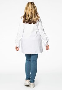 Biała koszula z długim rękawem o luźnym kroju i bufiastych rękawach, zestawiona z niebieskimi skinny jeansami i jasnymi sneakersami.