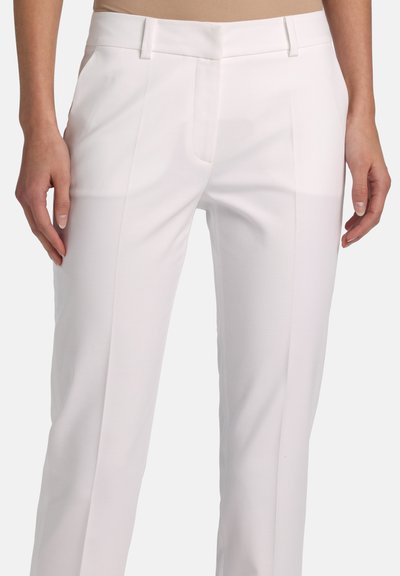 White tailored slim-fit trousers with front crease, mid-rise waist, and side pockets worn by a standing person with hands relaxed at sides.