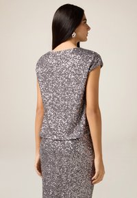 Srebrna, cekinowa bluzka z krótkim rękawem, okrągłym dekoltem i luźnym krojem, zestawiona z dopasowaną cekinową spódnicą, całość o teksturowanym połysku.