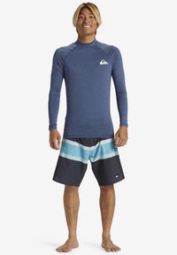 Ανδρική στολή για σερφ που αποτελείται από μπλουζάκι μακρυμάνικο μπλε με λογότυπο και μαύρο μαγιό βερμούδα με τιρκουάζ και λευκές ρίγες.