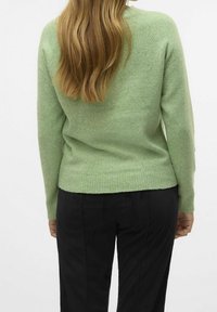 Pull en laine verte à texture finition, avec des manches longues et un ourlet côtelé. Associé à un pantalon en velours côtelé noir pour le contraste.