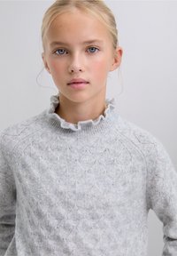 Suéter de punto gris claro con un patrón de rombos y un cuello con volantes. Textura suave, mangas largas y un ajuste informal.