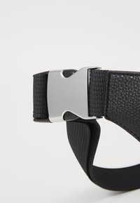 Black belt featuring a textured leather strap and a silver metal buckle. The design emphasizes a sleek, minimalist style with durable materials.