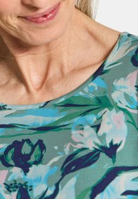 Bluse mit kurzen Ärmeln in Grün, mit blauen und rosa Blumenmustern, einem runden Ausschnitt und weichem Stoffgefühl.