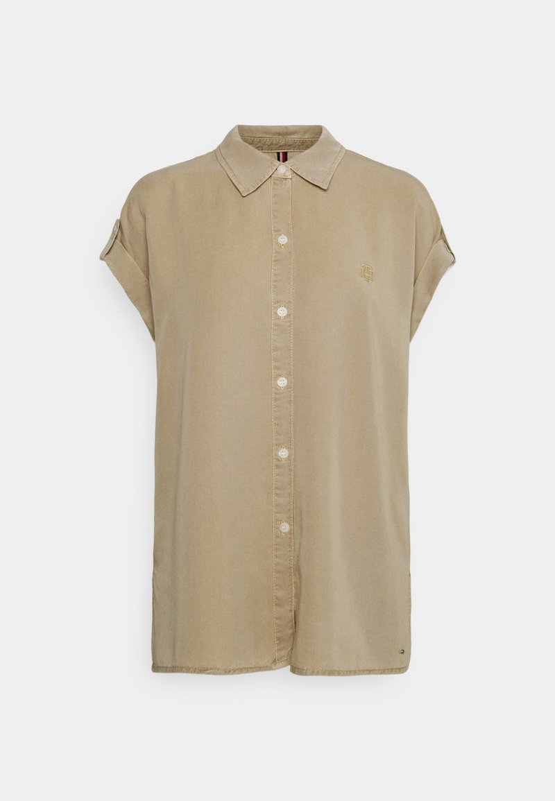 Chemise beige à manches courtes, boutonnée, avec col, manches retroussées et logo brodé discret sur le côté gauche de la poitrine.