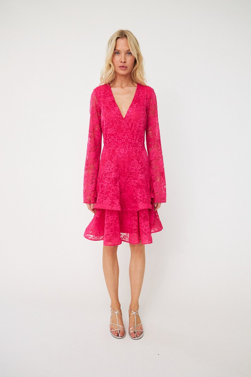 Rochie roz din dantelă cu mâneci lungi, decolteu adânc în V și fustă stratificată. Prezintă modele florale pe toată suprafața și este asortată cu sandale argintii cu barete.