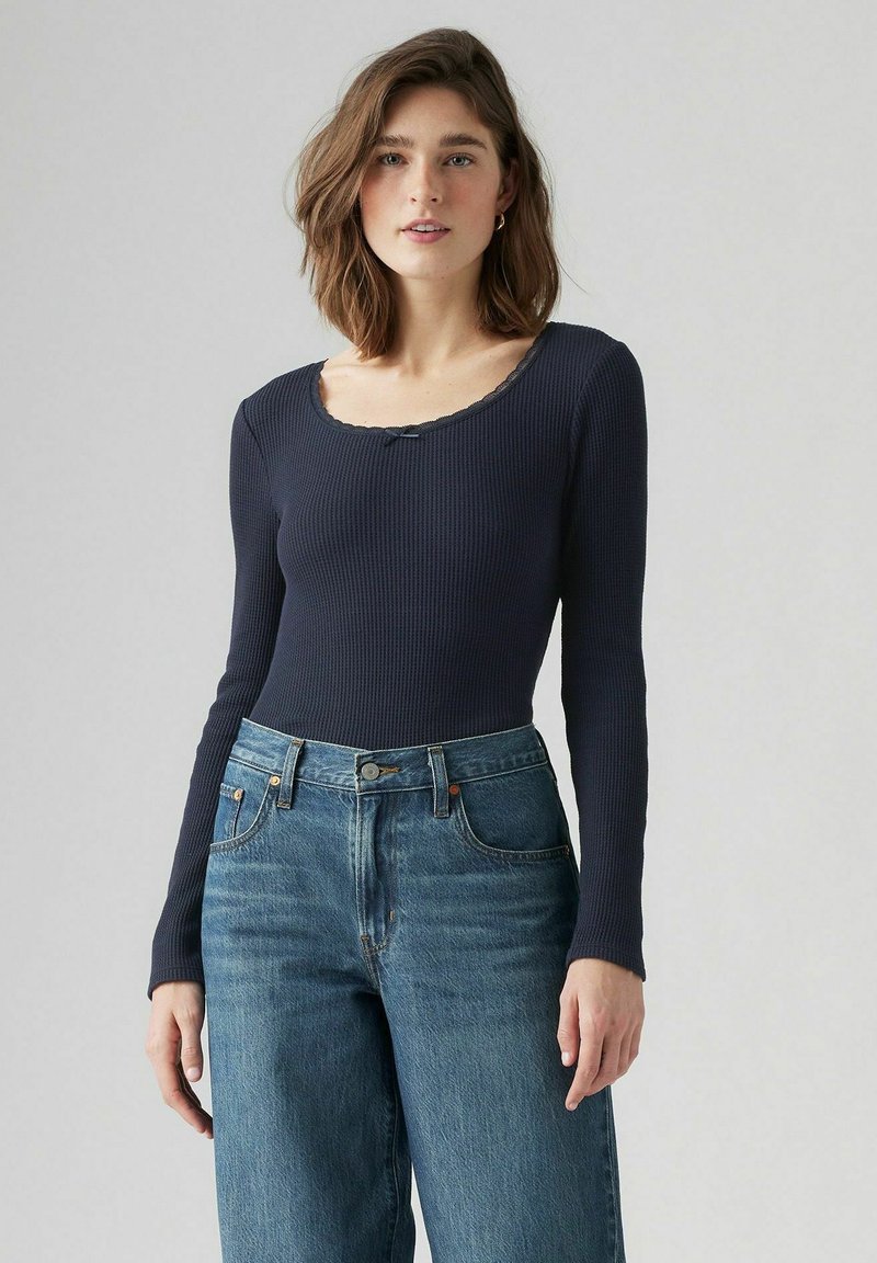 Marineblauw geribd T-shirt met lange mouwen en een ronde halslijn, voorzien van een delicate scalloped rand, gecombineerd met hooggerimpelde lichtblauwe jeans.