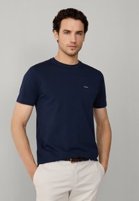 Granatowa bawełniana koszulka z okrągłym dekoltem i krótkimi rękawami, z małą kieszonką na lewej piersi oraz logo marki.