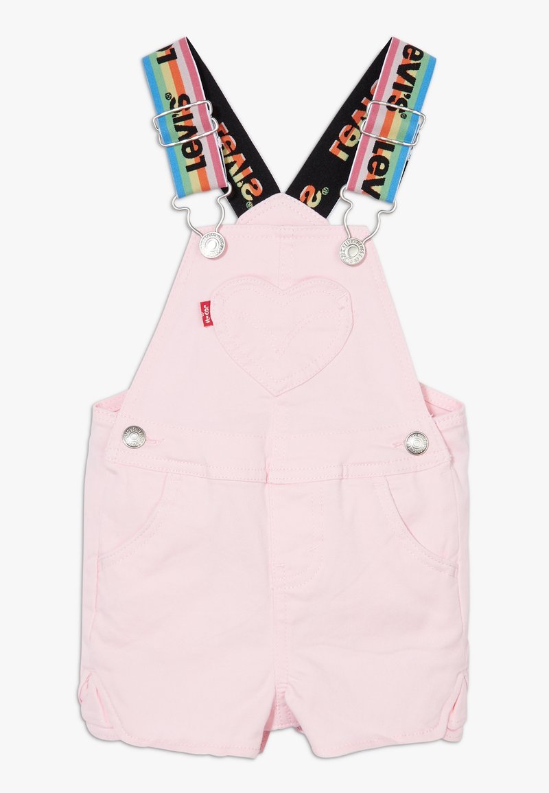 Salopette di jeans rosa con hardware argentato e dettagli cuciti a forma di cuore. Spallacci regolabili neri e a righe arcobaleno.